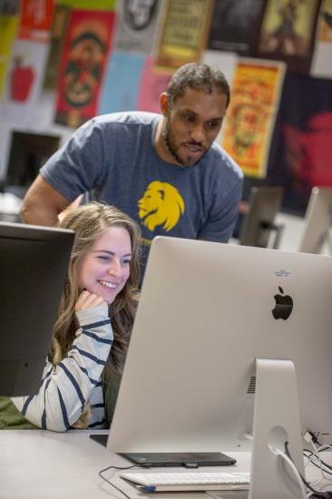 Teacher looking over the shoulder of a student using a computer.