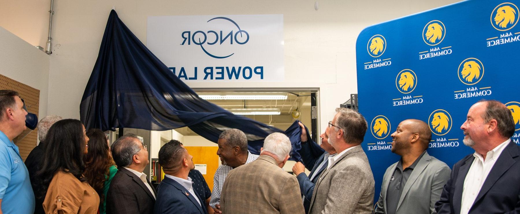 People look above doorway as curtain is pulled down to reveal "Oncor Power Lab" sign.