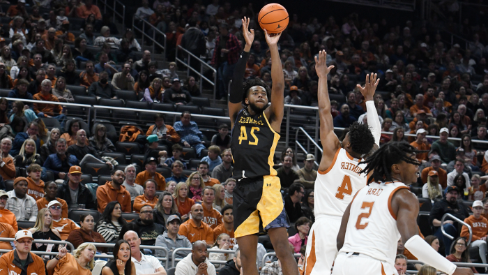 Player jumps to shoot the basketball ball while a second player blocks.